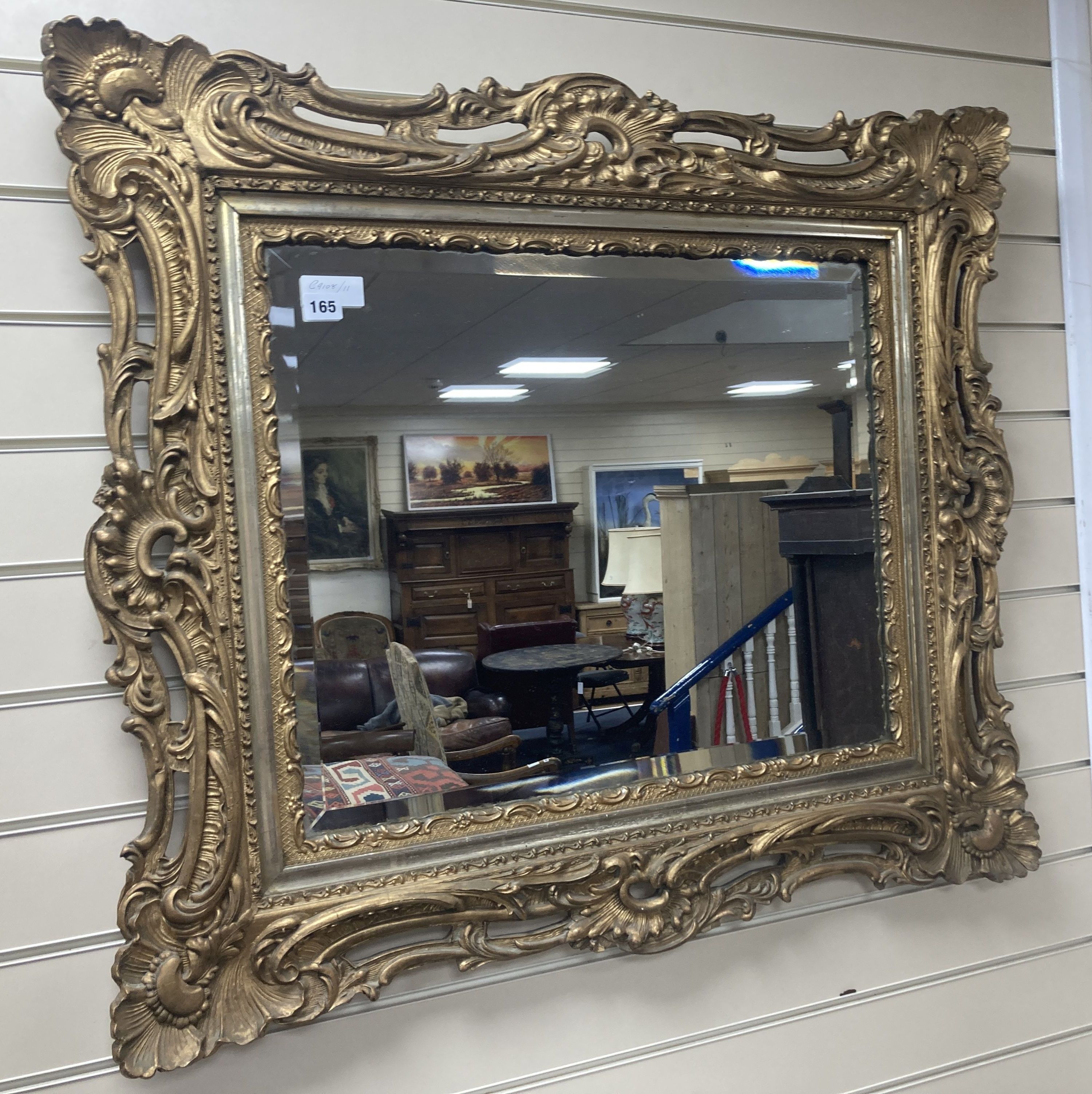 A rectangular carved and pierced framed gilt wall mirror in the rococo style, stepped and moulded border enclosing a bevelled plate, wi